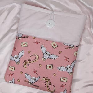 May include: Pink laptop sleeve featuring a white owl and lightning bolt design. The sleeve has a white button fastening.