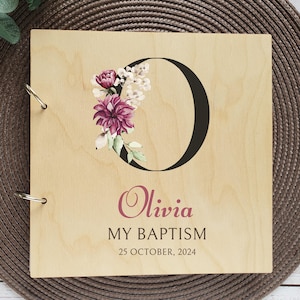 May include: A wooden photo album featuring a floral design and the letter "O" in black. The album is personalised with the name "Olivia" in pink lettering and the text "My Baptism" and "25 October, 2024" in black lettering.