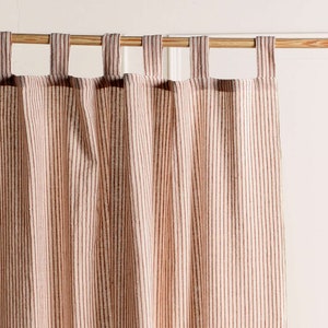 May include: A pair of cream-colored curtains with thin, brown stripes. The curtains are hung on a wooden rod with loops.