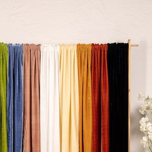 May include: A set of 10 velvet curtains in various colors, including burgundy, green, blue, pink, white, yellow, orange, and black. The curtains are hanging on a wooden rod and are arranged in a row.