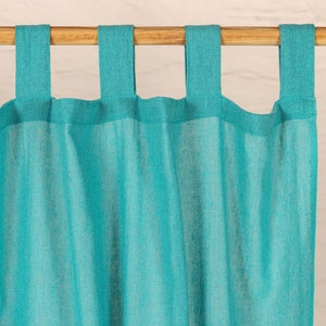 May include: Turquoise curtain panel with attached fabric loops for hanging. The curtain is made of a lightweight, textured fabric and hangs from a natural wood rod. The color is a vibrant teal, adding a pop of color to any room. Home decor.