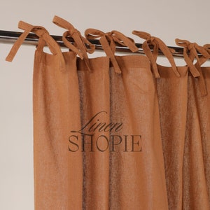 May include: A set of brown linen curtains with a tie-top design. The curtains are hung on a silver rod and have a subtle texture. The text "Linen Shopie" is printed on the curtains.