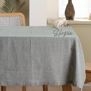 Könnte beinhalten: Eine weiße und graue gestreifte Tischdecke mit einem dezenten Glanz. Die Tischdecke liegt auf einem Holztisch mit einem Stuhl im Hintergrund.