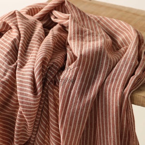 May include: A red and white striped throw blanket made of soft fabric. The blanket is folded and draped over a wooden surface.