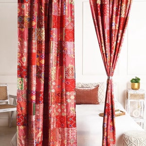 K&ouml;nnte beinhalten: Zwei rote Patchwork-Vorh&auml;nge mit geometrischem Muster h&auml;ngen an einer Gardinenstange. Die Vorh&auml;nge sind an beiden Seiten zur&uuml;ck gebunden und geben den Blick auf ein wei&szlig;es Bett mit roten Kissen frei.