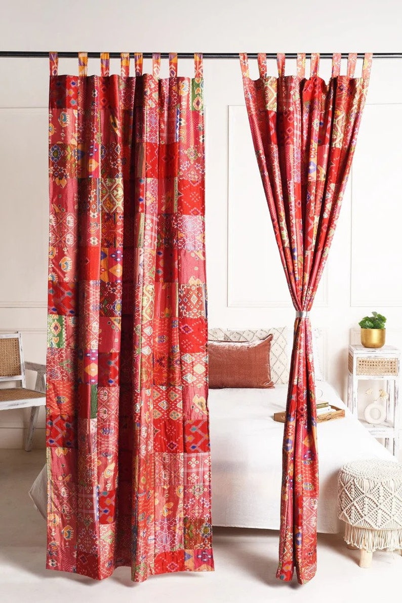 K&ouml;nnte beinhalten: Zwei rote Patchwork-Vorh&auml;nge mit geometrischem Muster h&auml;ngen an einer Gardinenstange. Die Vorh&auml;nge sind an beiden Seiten zur&uuml;ck gebunden und geben den Blick auf ein wei&szlig;es Bett mit roten Kissen frei.