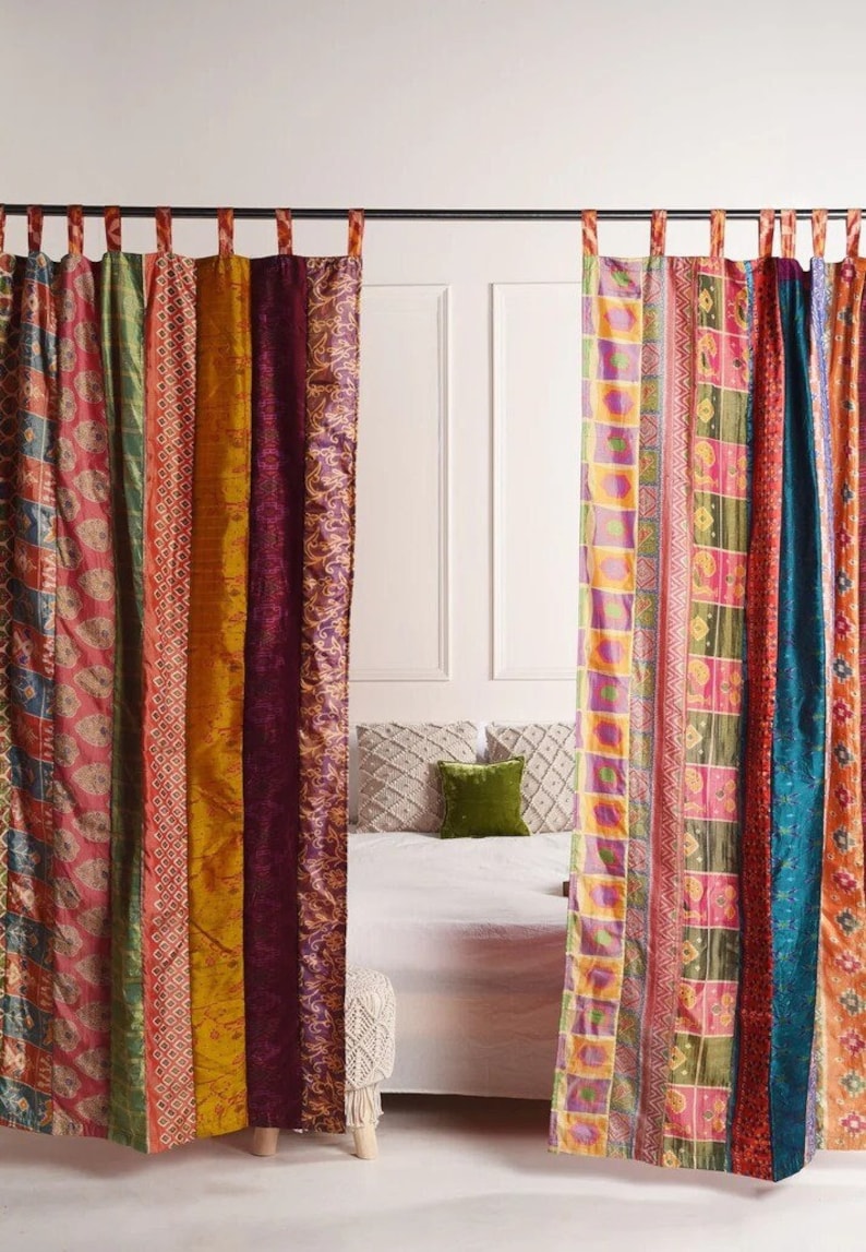 K&ouml;nnte beinhalten: Ein Paar bunte Vorh&auml;nge aus Patchwork-Stoff. Die Vorh&auml;nge sind an einer schwarzen Stange aufgeh&auml;ngt und zeigen eine Vielzahl von Mustern und Farben, darunter Rot, Gr&uuml;n, Gelb und Blau.