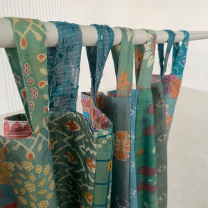 May include: A set of six colorful fabric curtains with a patchwork design, hanging from a white rod. The curtains are made of different fabrics with various patterns, including floral, geometric, and paisley.