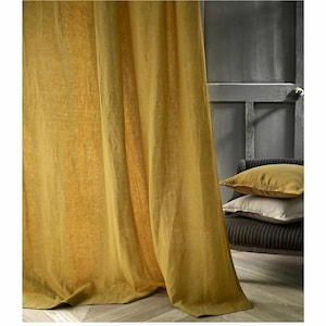 May include: A pair of mustard yellow linen curtains hanging in a room with a wooden floor. The curtains are gathered at the top and hang down to the floor.