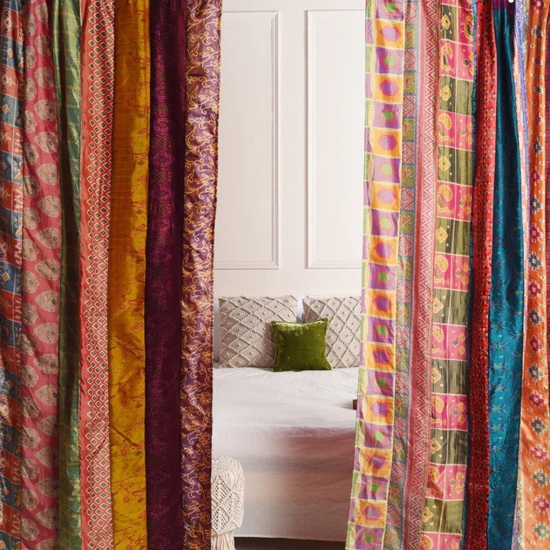 K&ouml;nnte beinhalten: Ein Satz farbenfroher Vorh&auml;nge aus Patchwork-Stoff mit verschiedenen Mustern und Texturen. Die Vorh&auml;nge h&auml;ngen in einem Raum mit einer wei&szlig;en Wand und einem Bett mit wei&szlig;en Bettw&auml;sche und Kissen.
