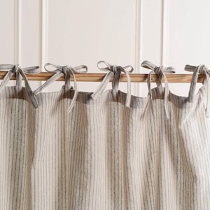 Könnte beinhalten: Beige und grau gestreifte Vorhangpaneele mit Bindebändern. Die Vorhänge hängen an einer Holzstange. Der Stoff hat vertikale Streifen in einer neutralen Farbpalette und schafft einen schlichten, eleganten Look für die Inneneinrichtung.
