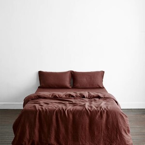 May include: A burgundy linen duvet cover with two matching pillowcases. The bedding is laid out on a wooden floor.