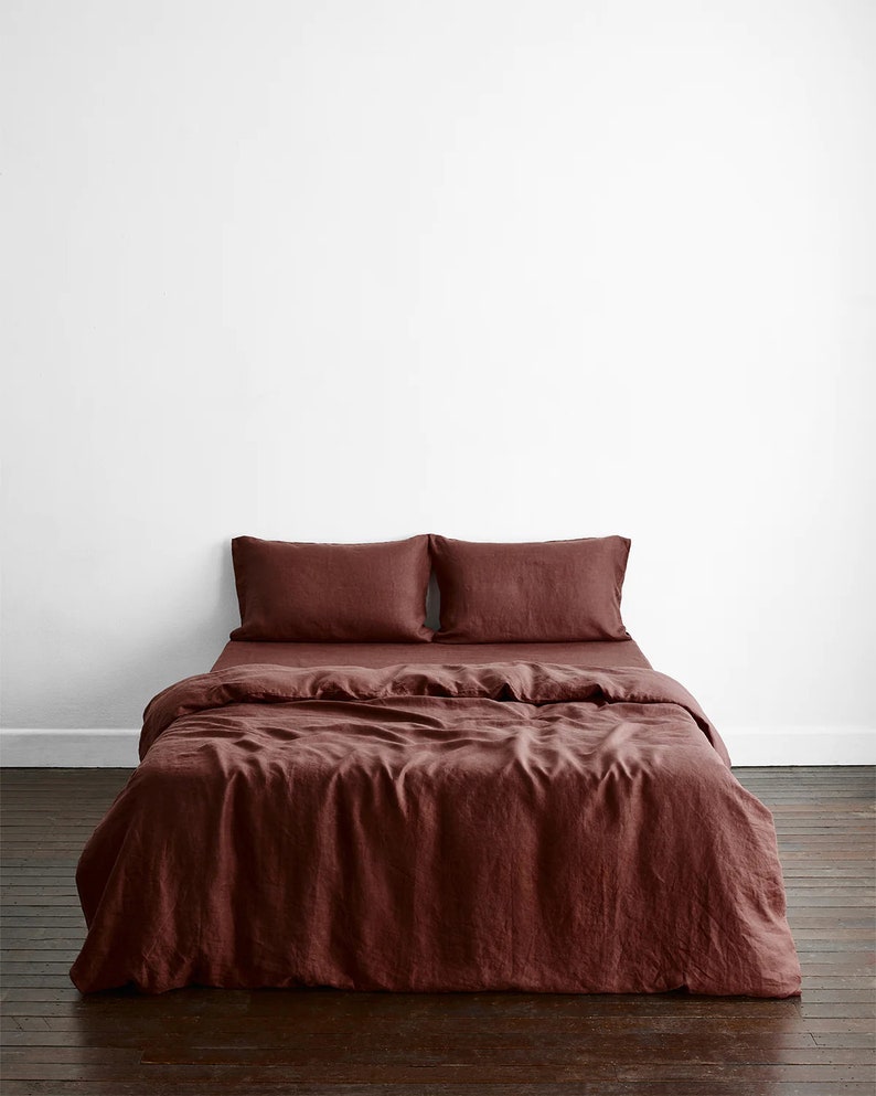 May include: A burgundy linen duvet cover with two matching pillowcases. The bedding is laid out on a wooden floor.
