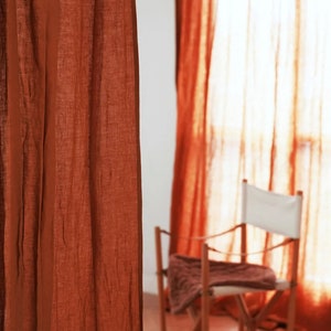 May include: A close-up of a rust-colored linen curtain with a wooden chair and a white balloon in the background.