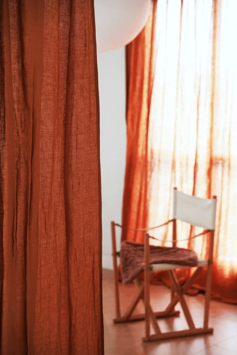 May include: A close-up of a rust-colored linen curtain with a wooden chair and a white balloon in the background.