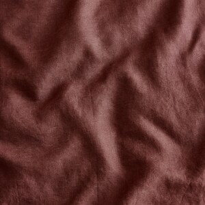 May include: A close-up of a deep burgundy fabric with a wrinkled texture. The fabric has a subtle sheen and a soft, smooth feel.