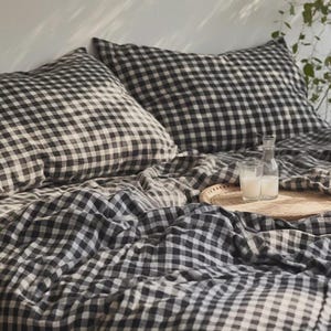 May include: Black and white gingham bedding with two pillows and a wooden tray with two glasses and a bottle on top.
