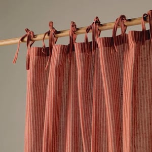 May include: Red and white striped curtains suspended from a wooden pole. The curtains are secured with fabric ties of a similar colour. The fabric has a textured finish, and the stripes run vertically.