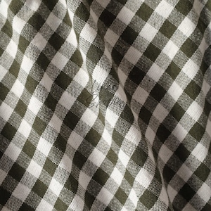 May include: Green and white gingham fabric with a diagonal pattern. The fabric is folded and has a soft, textured appearance.