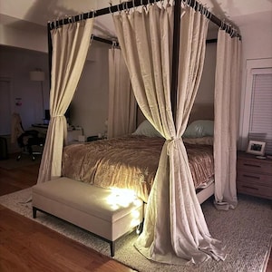 Può includere: Un letto a baldacchino bianco con un piumone in velluto marrone e un poggiapiedi bianco ai piedi del letto. Il letto si trova in una camera da letto con pavimento in legno e un tappeto.