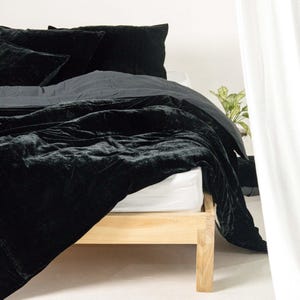 May include: A black velvet duvet cover and pillowcases on a wooden bed frame. The bedding is arranged in a simple and elegant way, with the duvet cover folded back to reveal the white sheets underneath.