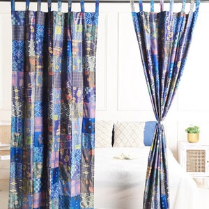 K&ouml;nnte beinhalten: Zwei blaue und violette Patchwork-Vorh&auml;nge mit geometrischem Muster. Die Vorh&auml;nge sind an einer Metallstange aufgeh&auml;ngt und mit Stoffb&auml;ndern zur&uuml;ckgebunden.