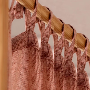 Puede incluir: Primer plano de un conjunto de cortinas de color óxido con un tejido tejido texturizado. Las cortinas están colgadas de una barra de madera.