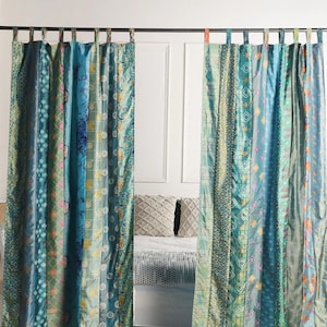 K&ouml;nnte beinhalten: Zwei t&uuml;rkisfarbene und gr&uuml;ne gemusterte Vorh&auml;nge mit Patchwork-Design h&auml;ngen an einer Gardinenstange. Die Vorh&auml;nge sind aus Seide und haben einen Boho-Stil.