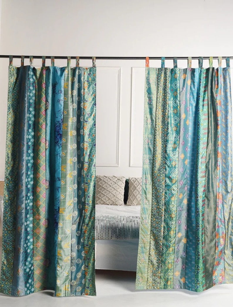 K&ouml;nnte beinhalten: Zwei t&uuml;rkisfarbene und gr&uuml;ne gemusterte Vorh&auml;nge mit Patchwork-Design h&auml;ngen an einer Gardinenstange. Die Vorh&auml;nge sind aus Seide und haben einen Boho-Stil.