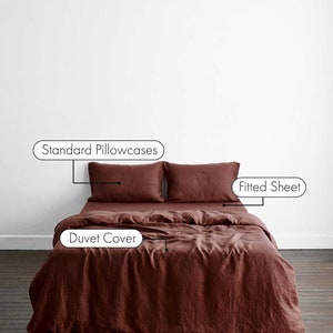 May include: A rust-coloured linen duvet cover with two standard pillowcases and a fitted sheet. The bedding is laid out on a wooden floor.
