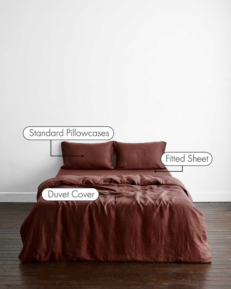 May include: A rust-coloured linen duvet cover with two standard pillowcases and a fitted sheet. The bedding is laid out on a wooden floor.