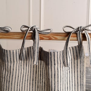 May include: Three white and black striped fabric panels with black fabric ties tied in bows. The panels are hanging from a wooden rod.