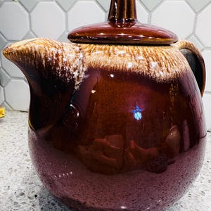 May include: A vintage brown ceramic teapot with a lid. The teapot has a glossy finish with a gradient of colors, from a light tan at the top to a deep brown at the base. The lid has a small handle.