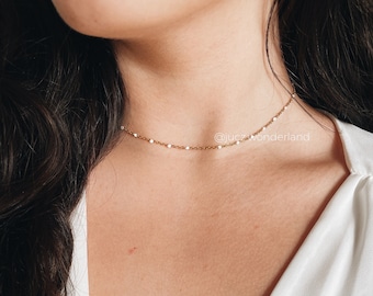 May include: A delicate gold chain choker necklace. The necklace is made of small, round beads and is very thin. The necklace is worn by a person with long dark hair and is sitting on a white background. The text "@jucz_wonderland" is visible in the image.