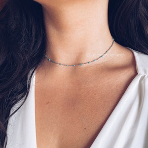 Op de afbeelding: Een zilveren choker ketting met turquoise kralen. De ketting wordt gedragen door een model dat een wit shirt draagt. De tekst "10-Turquoise silver" staat onderaan de afbeelding.