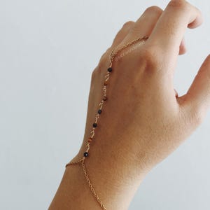 Puede incluir: Pulsera de cadena dorada con cuentas de ojo de tigre y negras. La pulsera está diseñada para usarse en la muñeca y el dedo, con una cadena que conecta las dos.