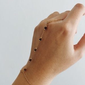 Può includere: Un braccialetto a catena dorata con perline marroni, indossato su una mano. Il braccialetto si estende lungo il braccio e termina con un anello sull'indice. Il testo '@jucz_wonderland' è visibile sulla mano.