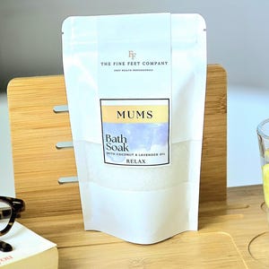 Peut inclure: Pochette blanche avec une étiquette qui indique "The Fine Feet Company Foot Health Professionals" et "Mums Bath Soak with Coconut & Lavender Oil Relax".