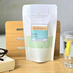Peut inclure: Une pochette blanche avec une étiquette verte qui dit "AUNTIES Bath Soak with Peppermint & Tea Tree REFRESH" et le logo "FF THE FINE FEET COMPANY FOOT HEALTH PROFESSIONALS".