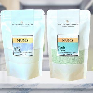 Peut inclure: Deux sachets blancs avec des étiquettes vertes et bleues. Les étiquettes indiquent "MUMS Bath Soak" avec le texte "RELAX" et "REFRESH" en dessous. Le sachet de gauche porte le texte "WITH COCONUT & LAVENDER OIL" et le sachet de droite porte le texte "WITH PEPPERMINT & TEA TREE".