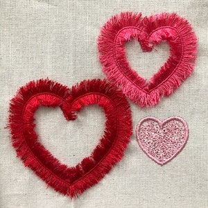Op de afbeelding: Drie geborduurde harten met gefranst randen. Het grootste hart is rood, het middelste hart is roze en rood, en het kleinste hart is roze.