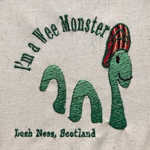 May include: Embroidered patch with a green, cartoon-style Loch Ness Monster wearing a red and white striped hat. The text "I'm a wee Monster, Loch Ness, Scotland" is stitched around the monster.