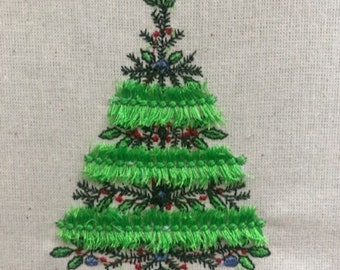 May include: Embroidered Christmas tree design on a light beige fabric. The tree features green fringe-like layers, red berry accents, and dark green needle-like branches. Small blue accents are also present, creating a festive holiday theme.