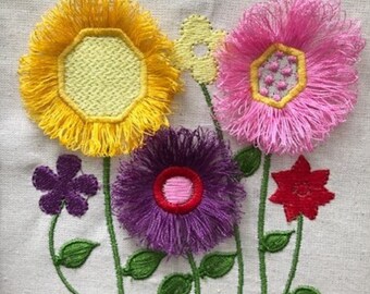 May include: Embroidered floral design with yellow, pink, purple, and red flowers. The flowers have a fringed edge and are surrounded by green leaves.