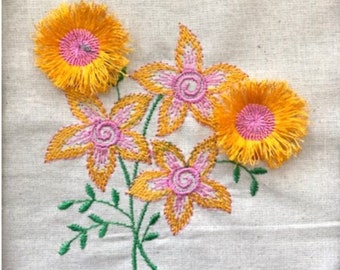May include: Embroidered floral design featuring yellow and pink flowers with green stems and leaves on a white fabric background.