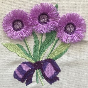 May include: Embroidered purple flowers with green stems and leaves tied together with a purple bow.