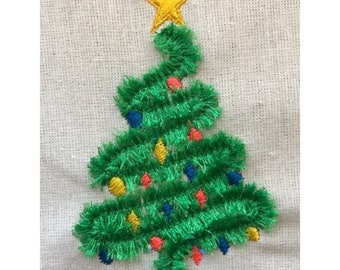 May include: Embroidered Christmas tree with a yellow star on top. The green tree is decorated with colorful lights in red, blue, and yellow. The embroidery is on a beige fabric background.