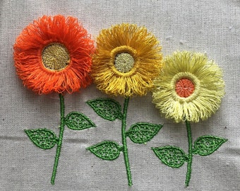 May include: Three embroidered flowers with green stems and leaves. The flowers are orange, yellow, and cream with a yellow center.