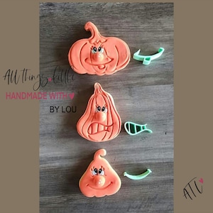 May include: Three orange pumpkin-shaped cookie cutters with embossed facial features, each accompanied by a small light green plastic piece. The text "All things little HANDMADE WITH BY LOU" and "ATL" is visible on the left and bottom right.