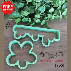 May include: Two light green plastic cookie cutters. One is a four-leaf clover shape, and the other is a rectangular shape with a scalloped edge. The text "All things little, handmade with love by Lou" is visible.